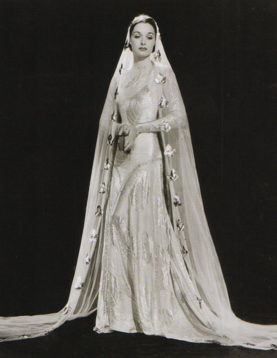 1930s fashion portrait, Wedding dress in bias cut silk with large self coloured leaf design in contrast texture. The veil is decorated with gold rosettes. 1930s fashion portrait, Wedding dress in bias cut silk with large self coloured leaf design in contrast texture. The veil is decorated with gold rosettes.